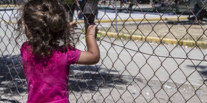 Girl with her back to the camera holding onto a wire fence